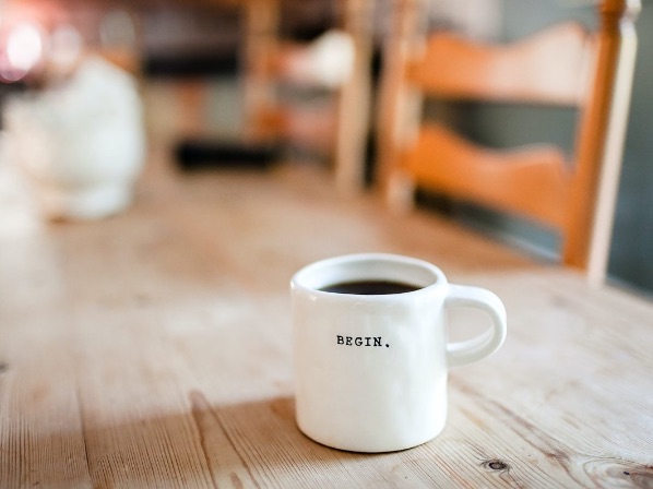 A mug with coffee or tea with the word "begin" printed on it.
